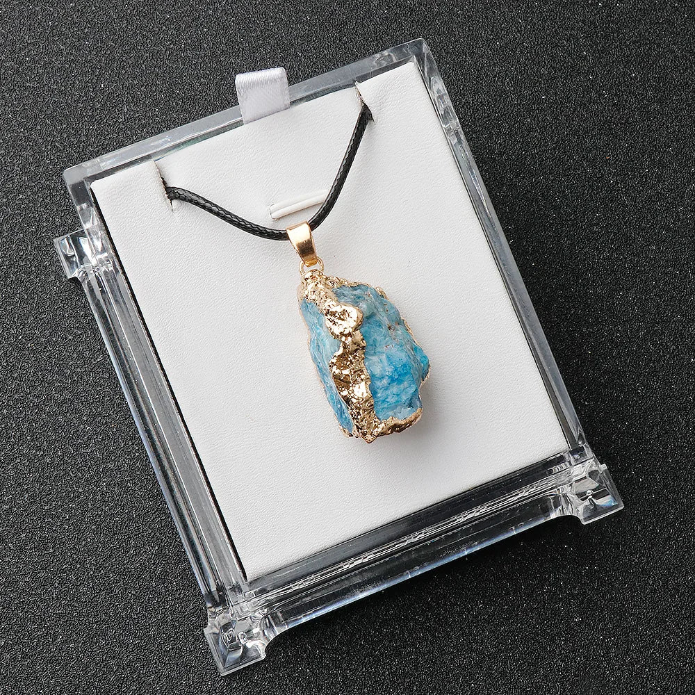 Blue stone pendant with gold accents on a black cord, displayed in a clear box.