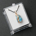 Blue stone pendant with gold accents on a black cord, displayed in a clear box.